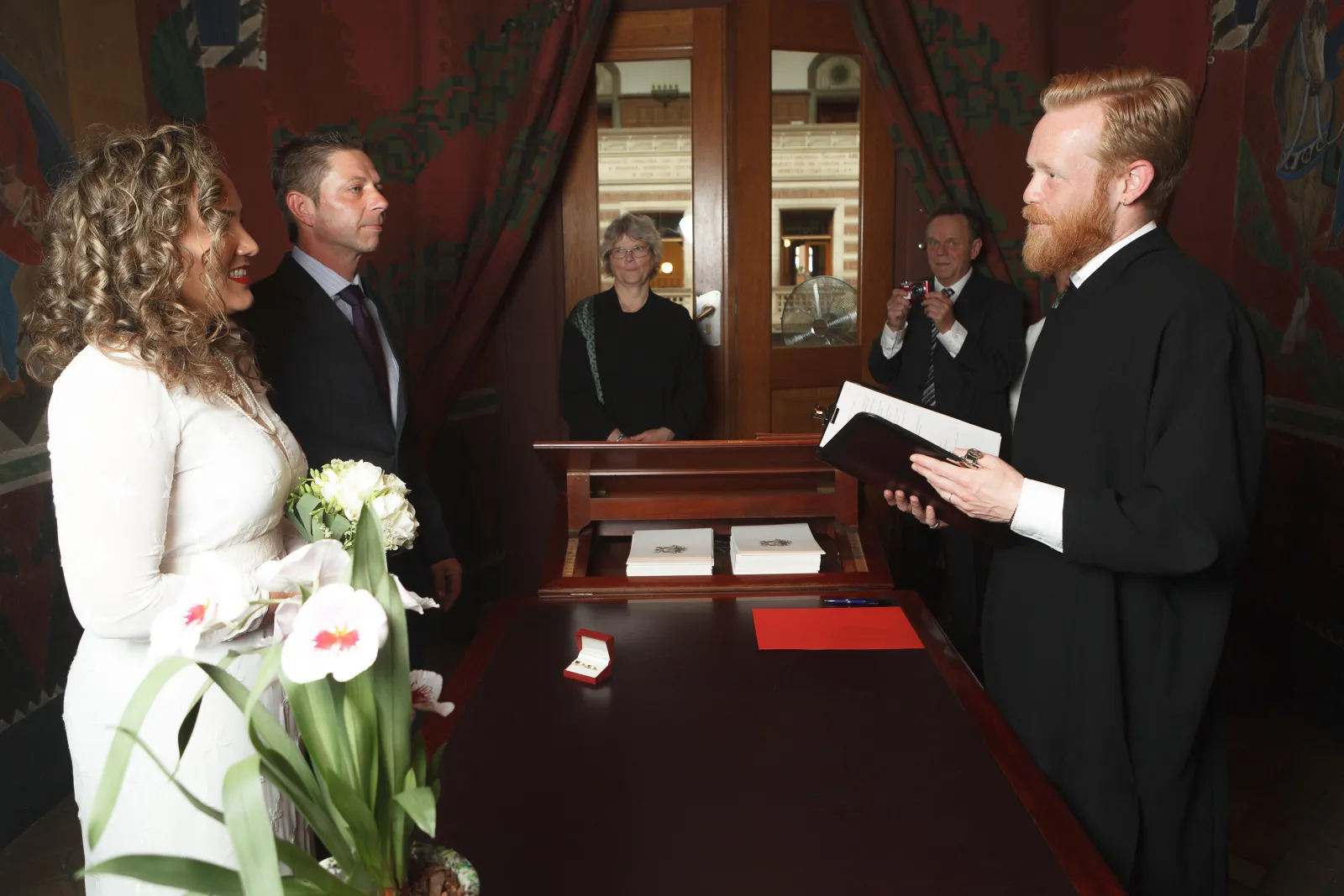 Eine Braut steckt dem Bräutigam den Hochzeitring an dem Finger in einem Standesamt